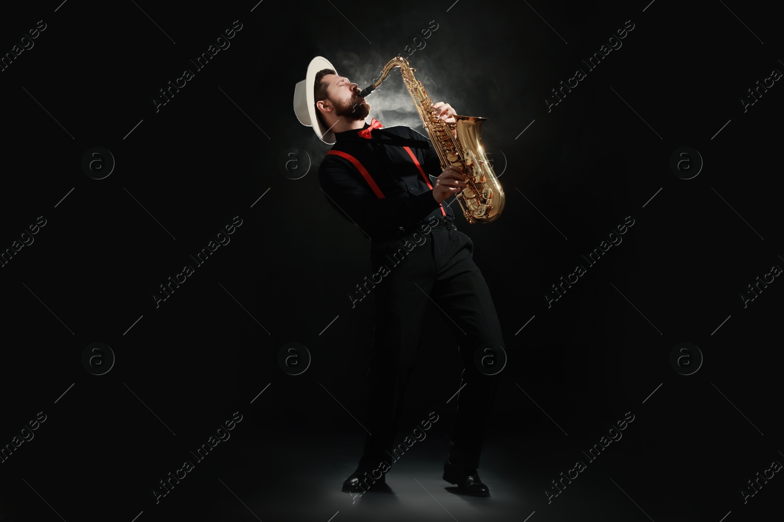 Photo of Professional musician playing saxophone on black background with smoke