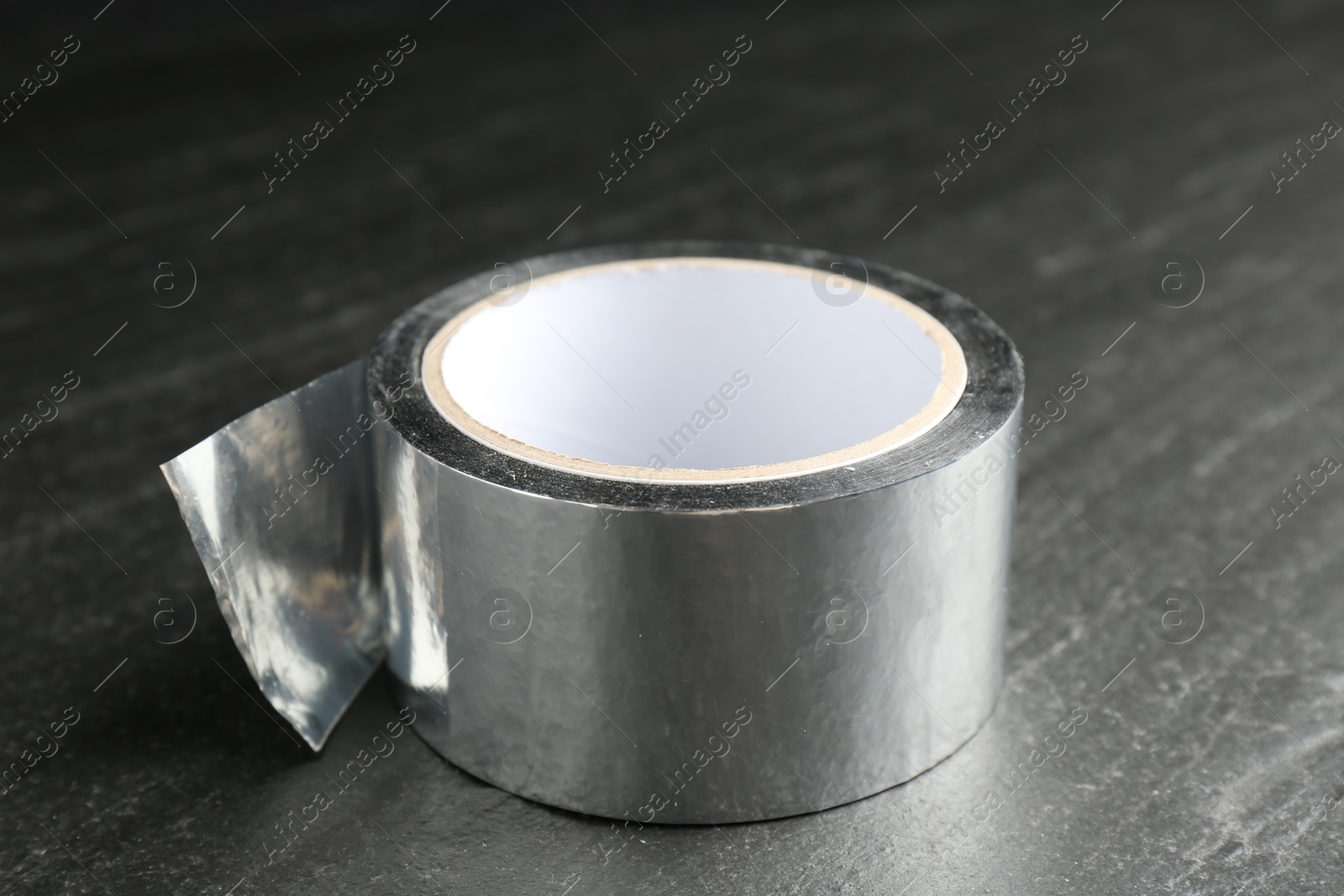 Photo of Roll of silver adhesive tape on black table, closeup