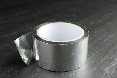 Roll of silver adhesive tape on black table, closeup