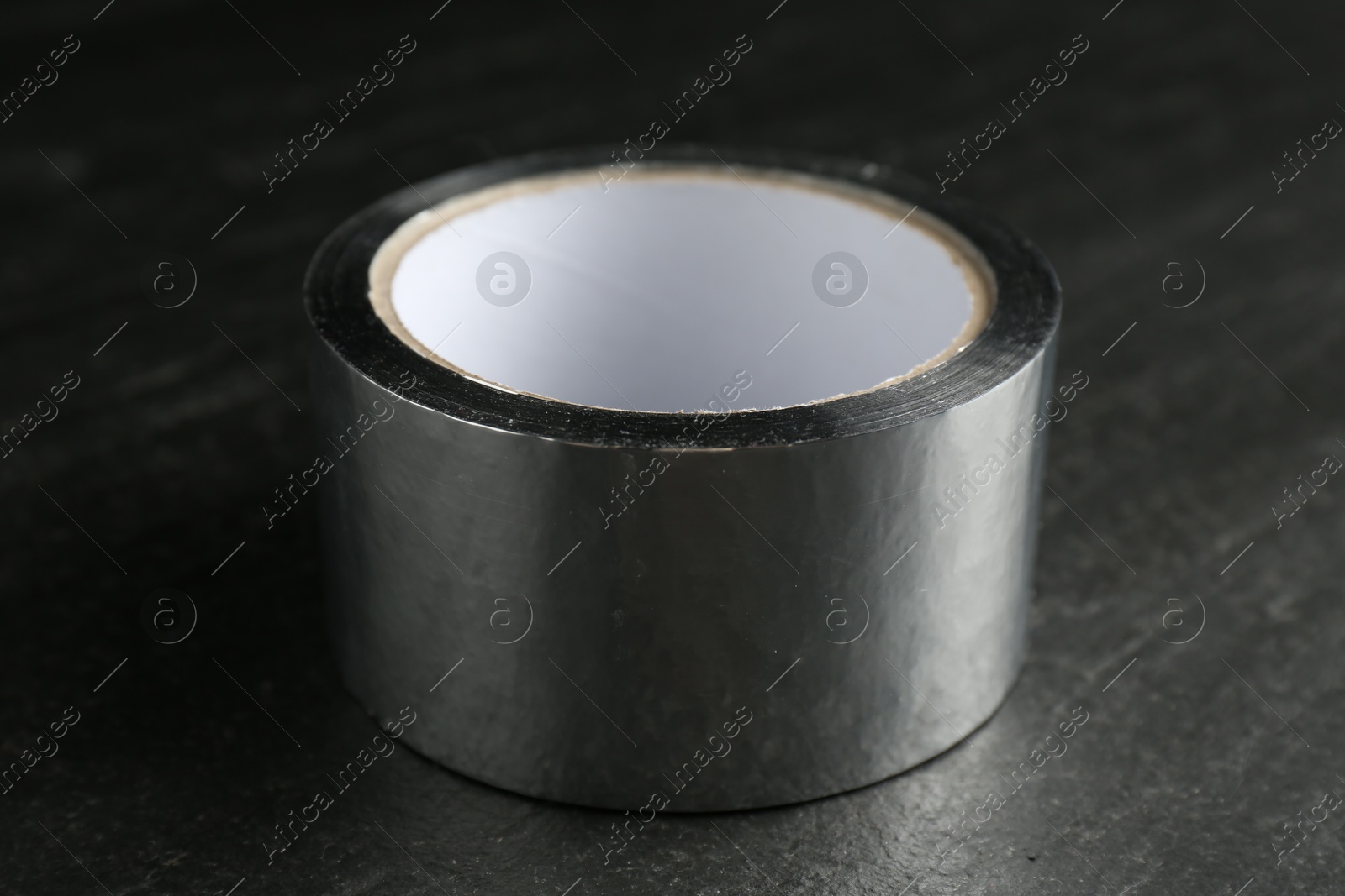 Photo of Roll of silver adhesive tape on black table, closeup