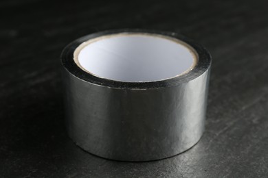 Roll of silver adhesive tape on black table, closeup