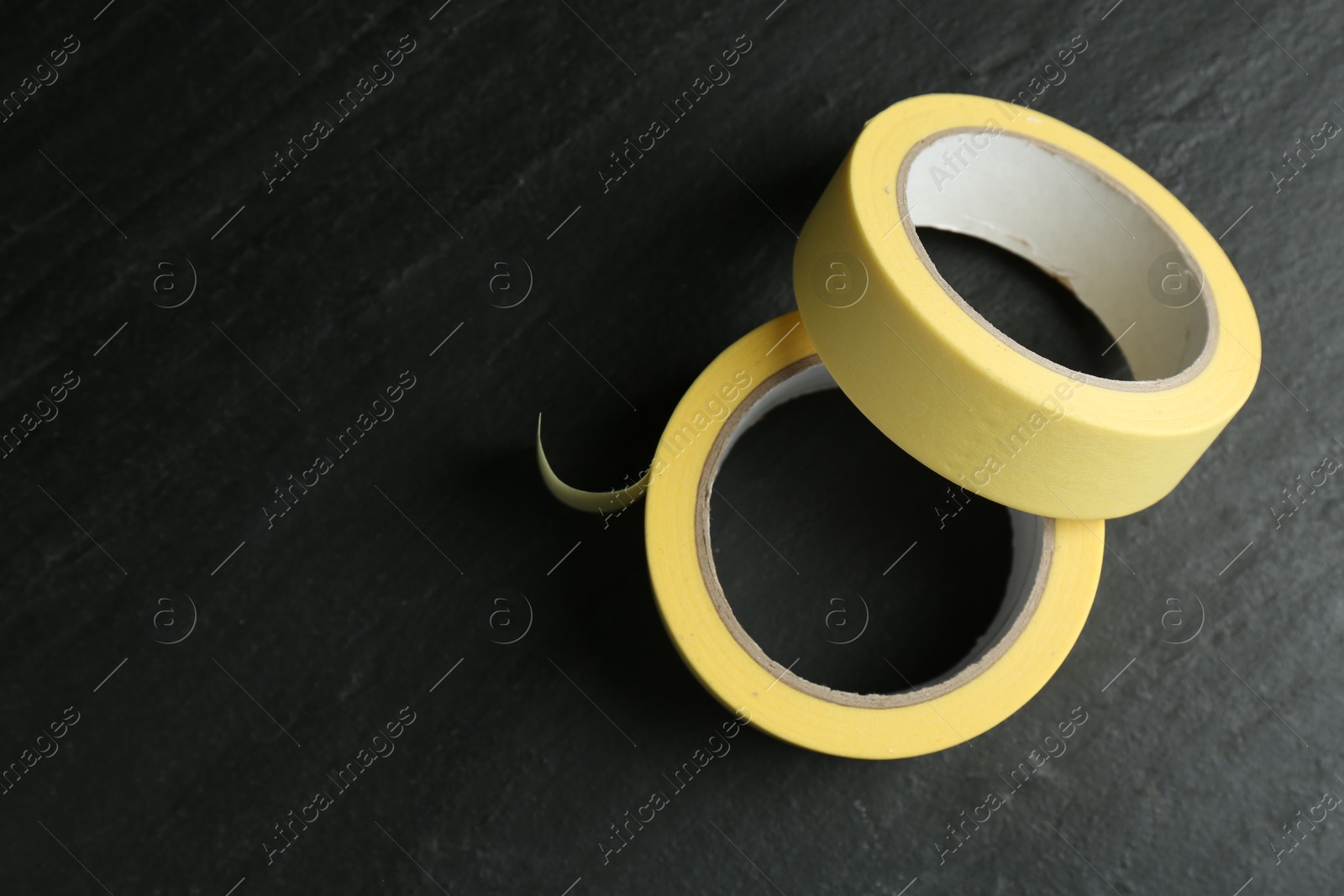 Photo of Rolls of masking tape on black table, top view. Space for text