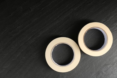 Photo of Rolls of masking tape on black table, top view. Space for text