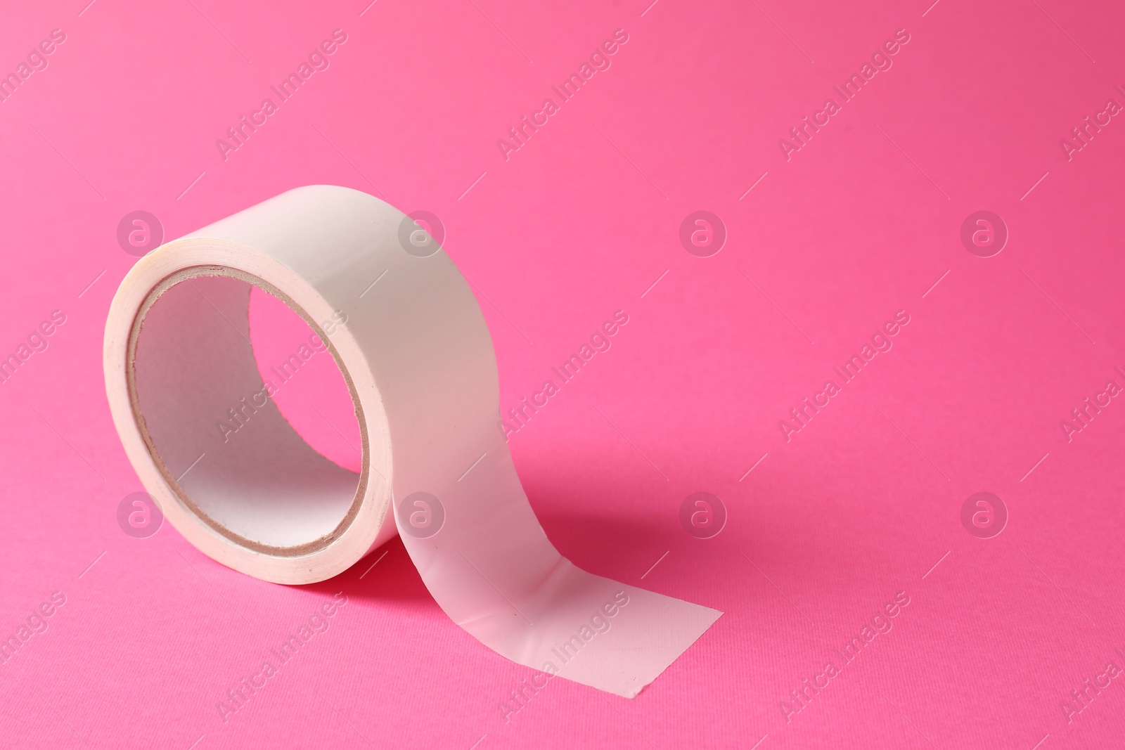 Photo of One masking tape on pink background, closeup. Space for text