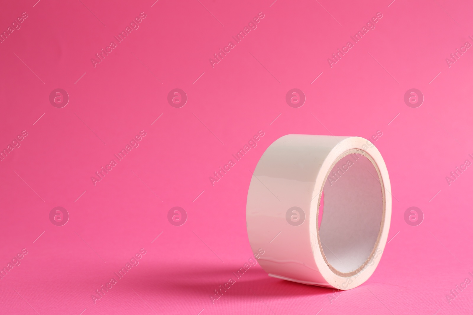 Photo of One masking tape on pink background, closeup. Space for text