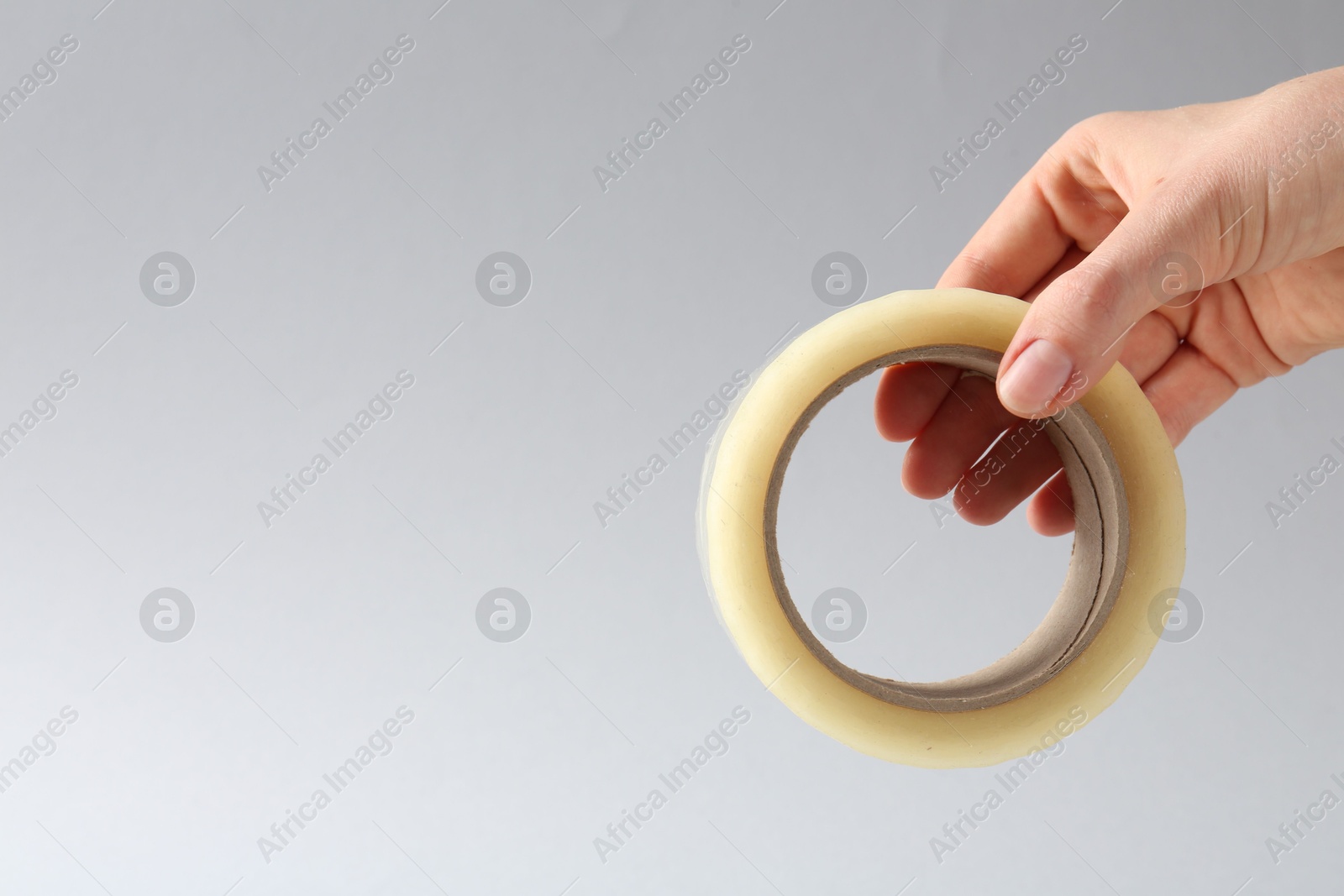 Photo of Woman holding masking tape on grey background, closeup. Space for text