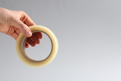 Woman holding masking tape on grey background, closeup. Space for text