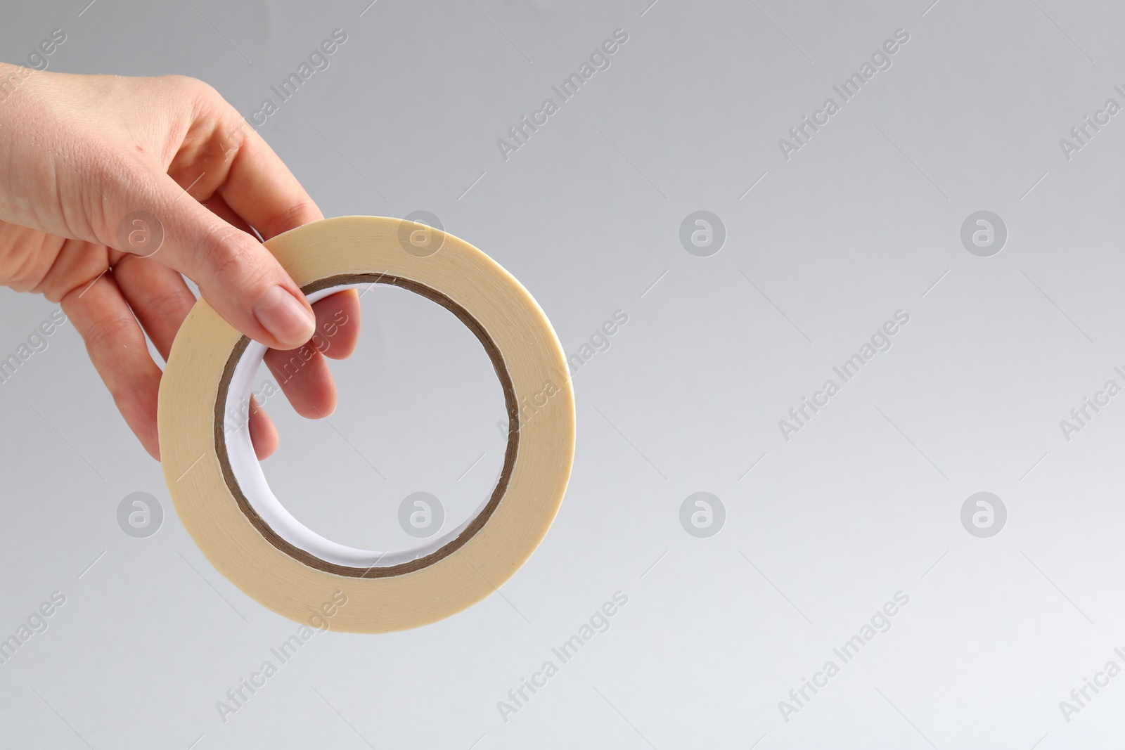 Photo of Woman holding masking tape on grey background, closeup. Space for text