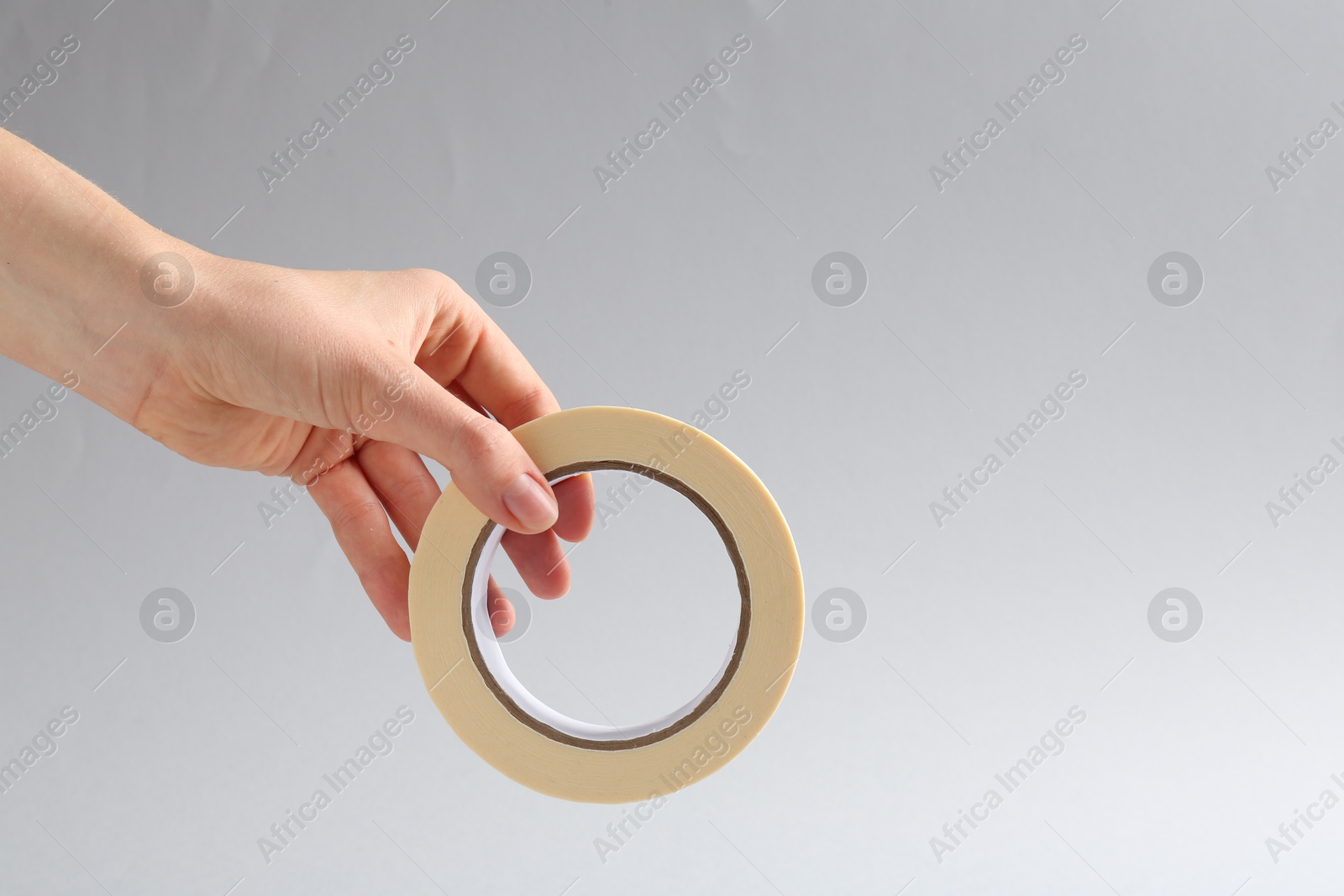 Photo of Woman holding masking tape on grey background, closeup. Space for text