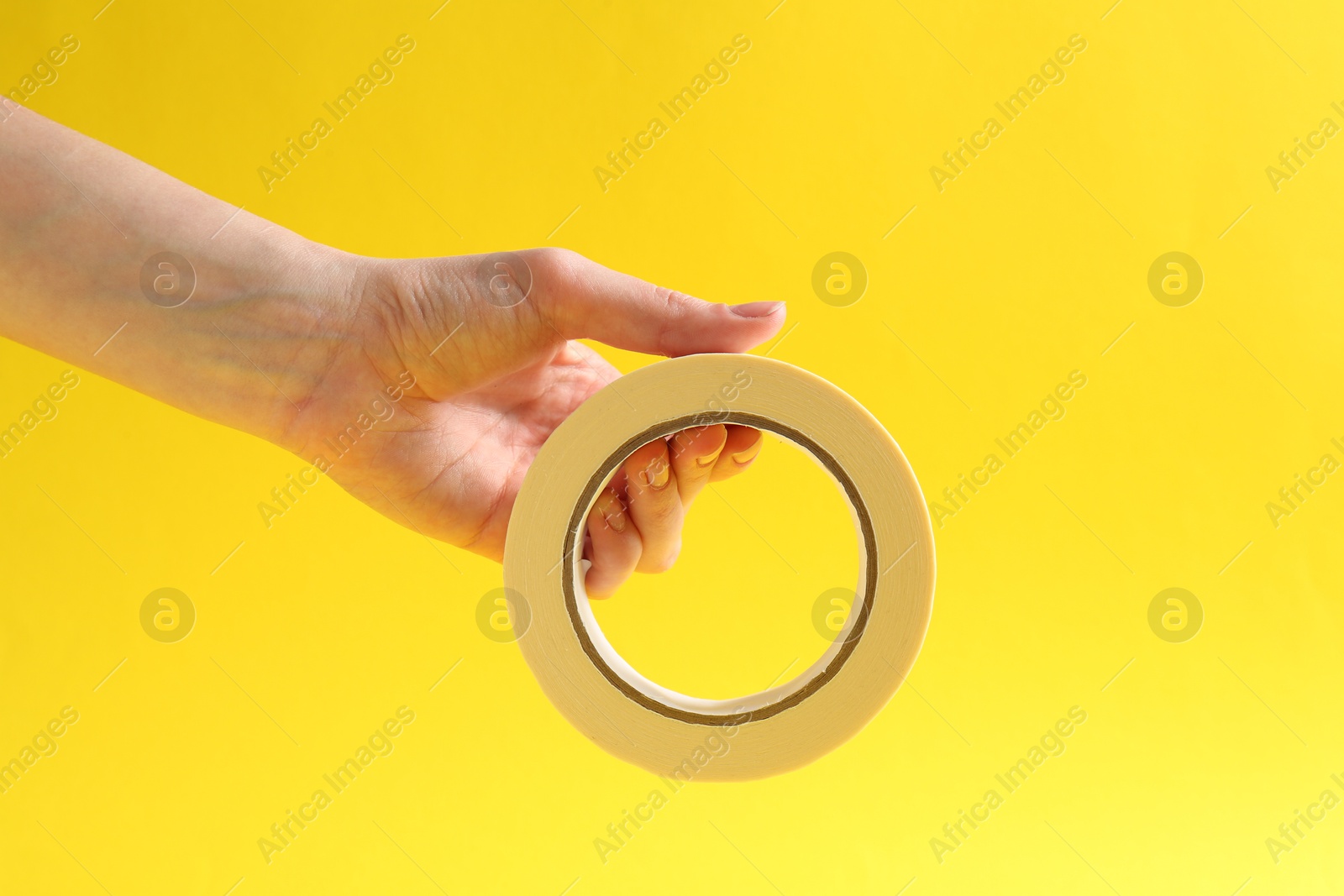 Photo of Woman holding masking tape on yellow background, closeup. Space for text