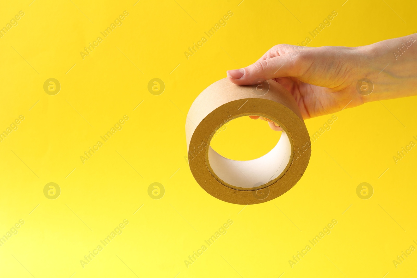 Photo of Woman holding masking tape on yellow background, closeup. Space for text