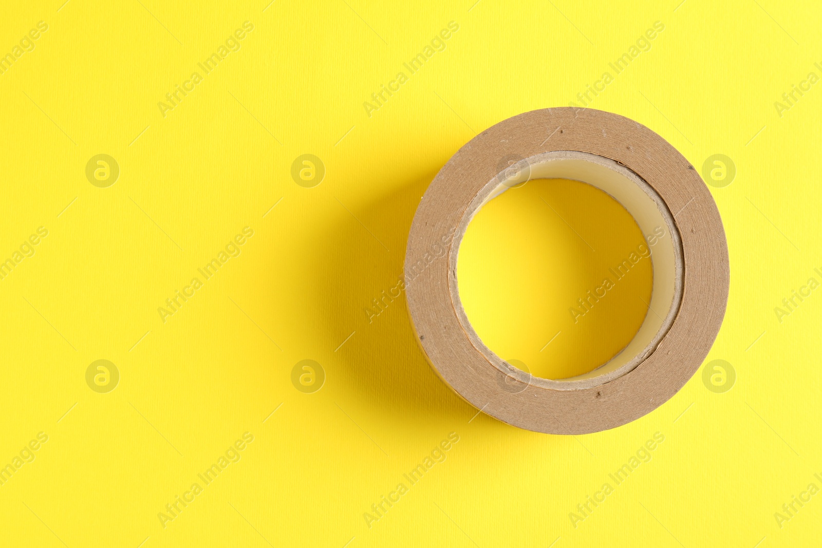 Photo of One masking tape on yellow background, top view. Space for text