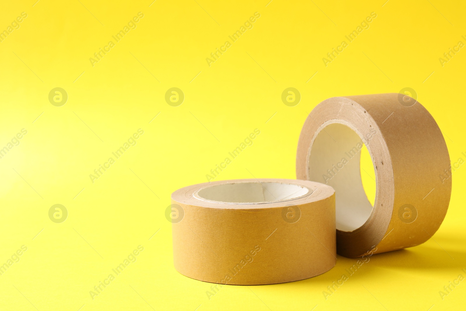 Photo of Two masking tapes on yellow background, closeup. Space for text