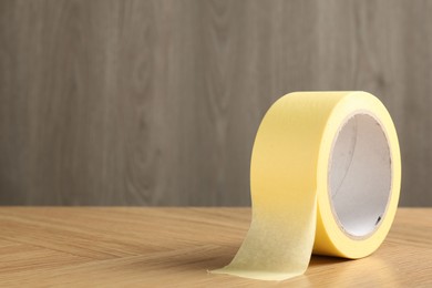 One masking tape on wooden table, closeup. Space for text