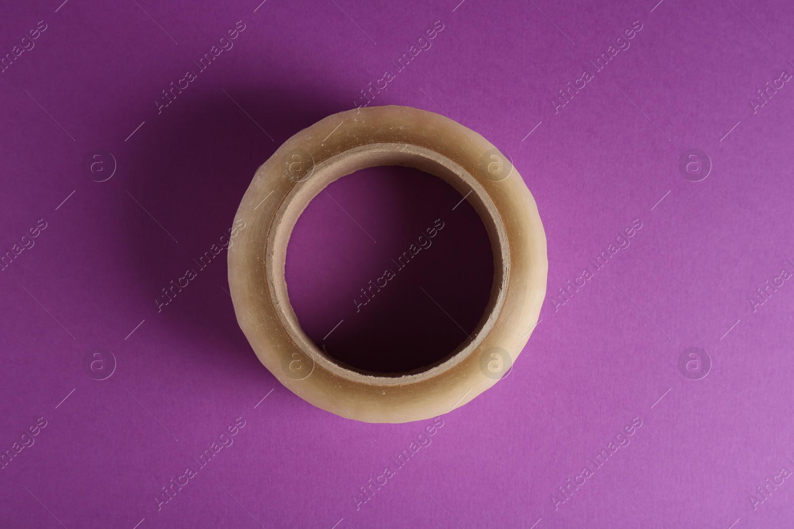 Photo of Roll of masking tape on violet background, top view