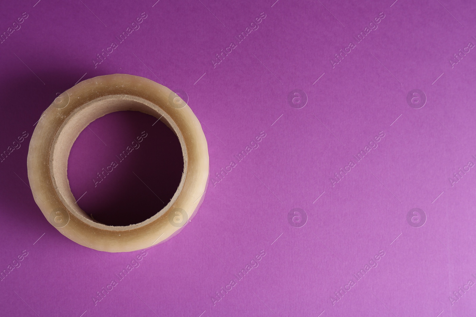 Photo of Roll of masking tape on violet background, top view. Space for text