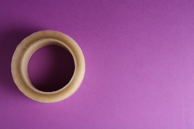 Photo of Roll of masking tape on violet background, top view. Space for text