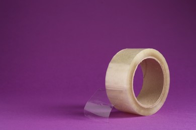 Photo of Roll of adhesive tape on violet background, space for text