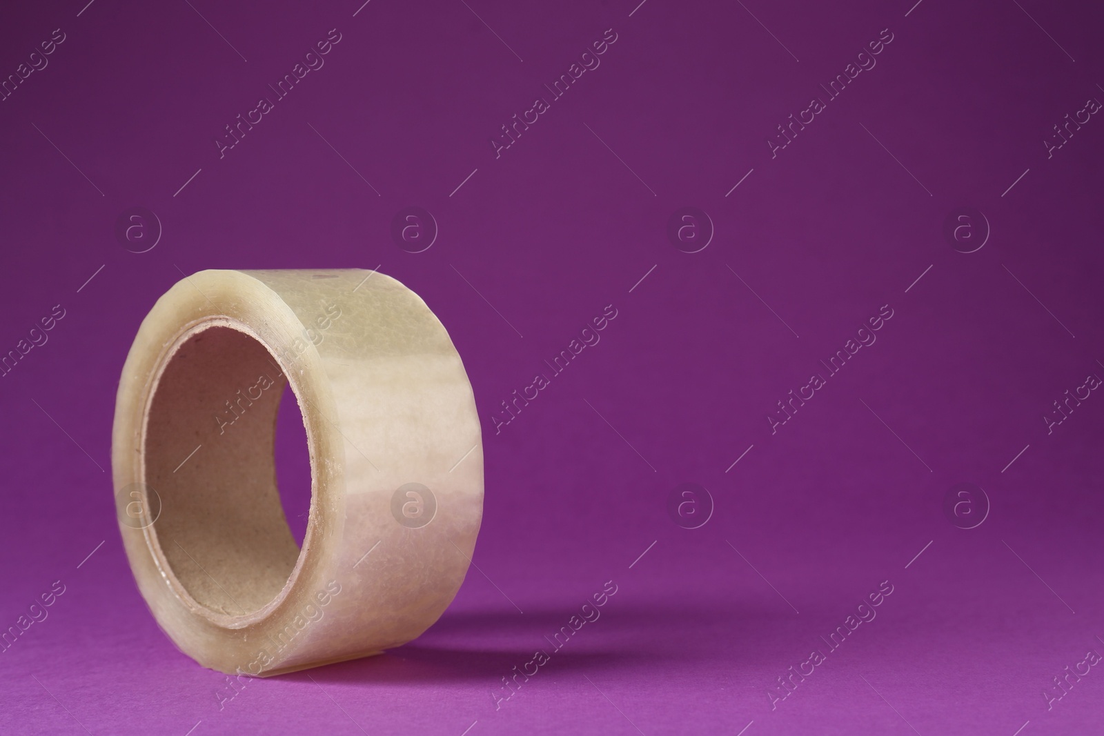 Photo of Roll of adhesive tape on violet background, space for text