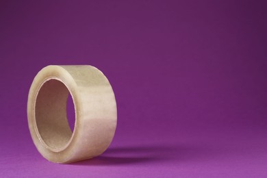 Photo of Roll of adhesive tape on violet background, space for text