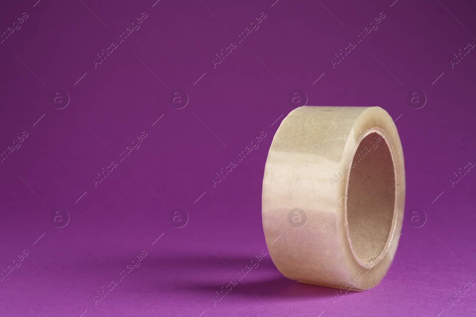 Photo of Roll of adhesive tape on violet background, space for text