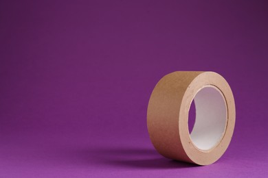 Photo of Roll of masking tape on violet background, space for text