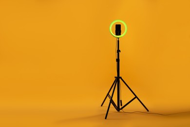 Photo of Ring lamp with smartphone on orange background, space for text