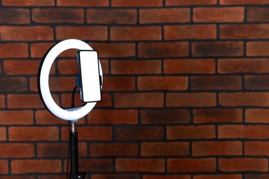 Photo of Ring lamp with smartphone against brick wall, space for text