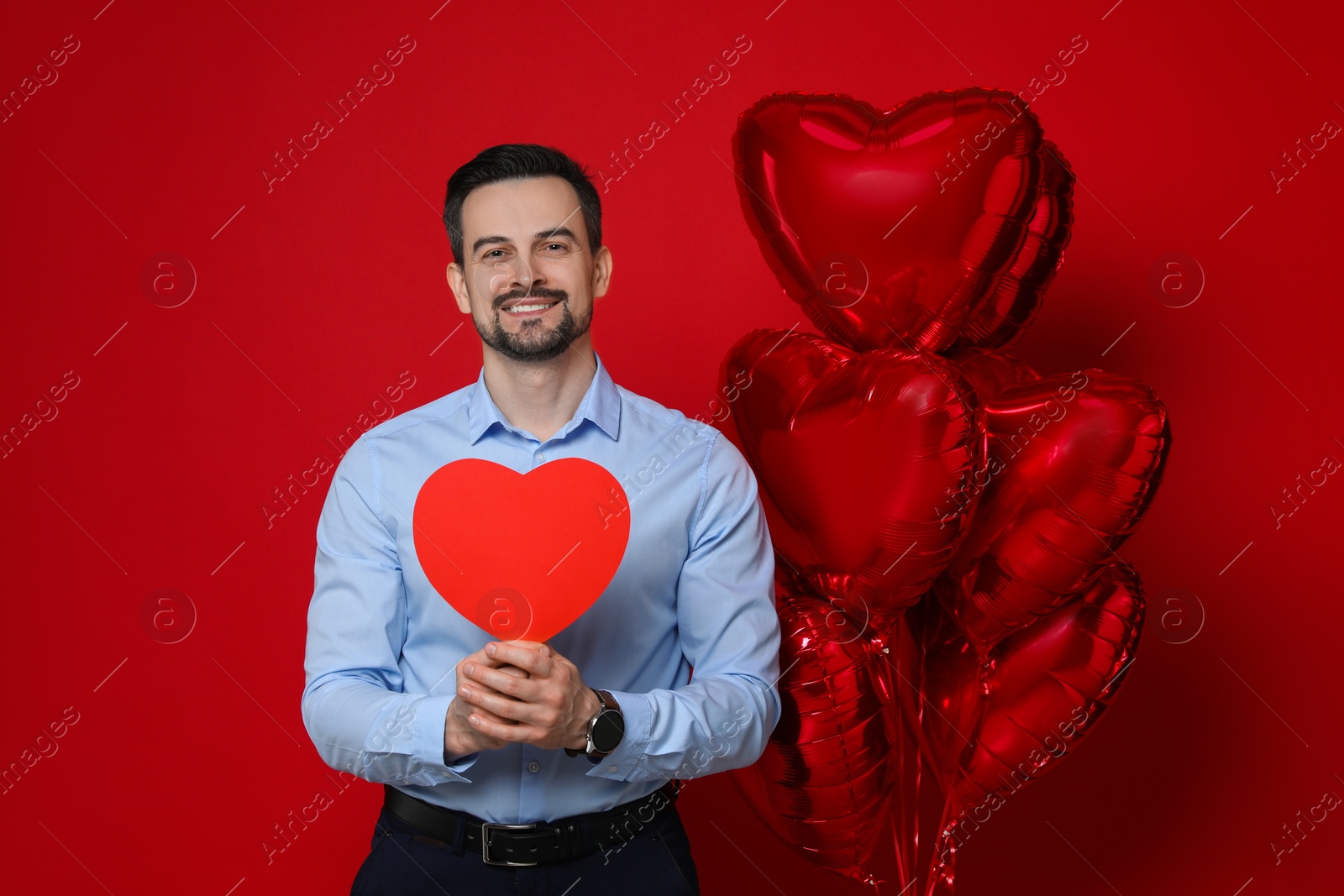 Photo of Happy Valentine's Day. Handsome man with paper heart and balloons on red background