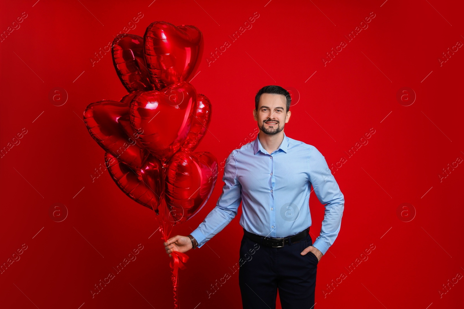 Photo of Happy Valentine's Day. Handsome man with heart shaped balloons on red background