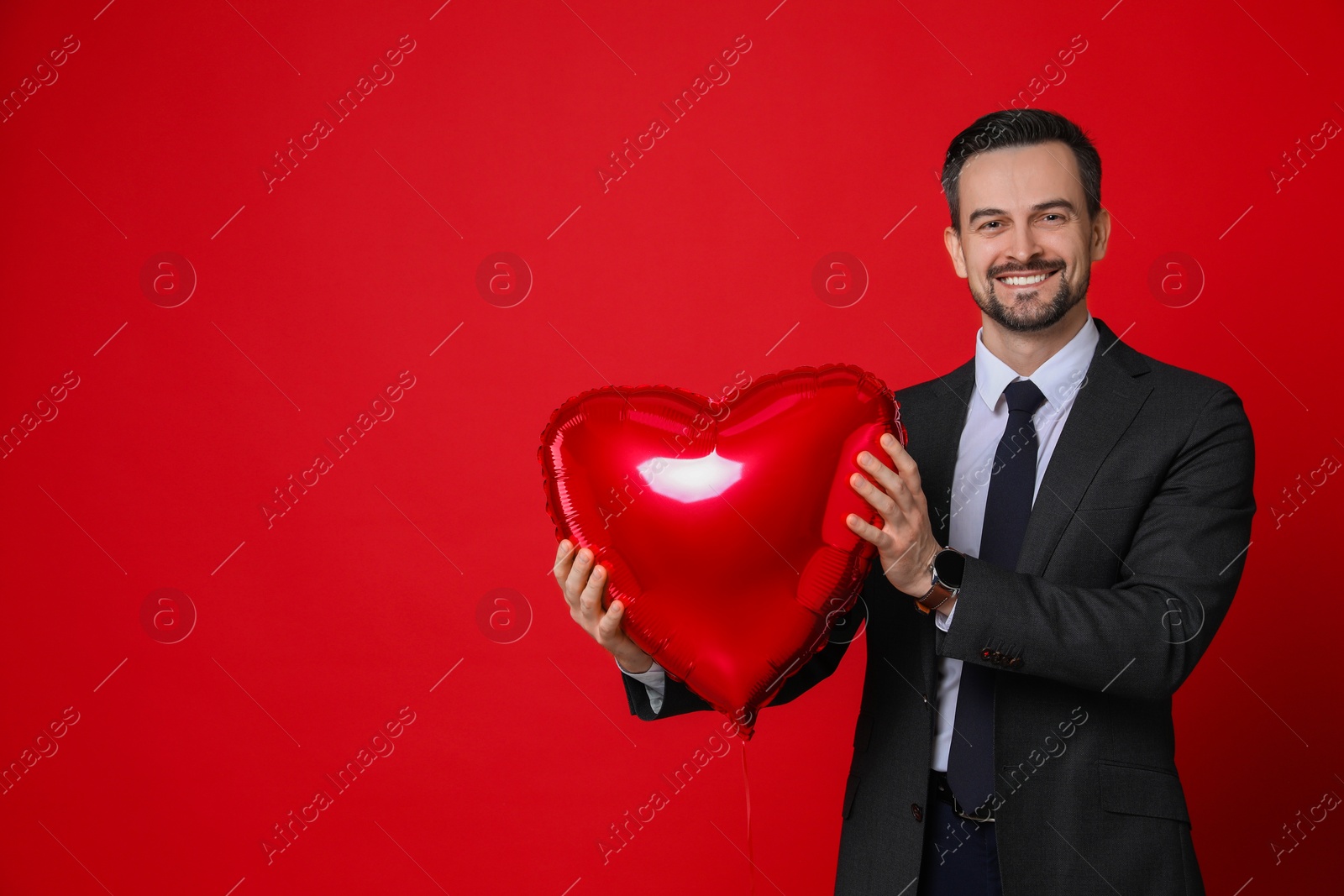 Photo of Happy Valentine's Day. Handsome man with heart shaped balloon on red background. Space for text