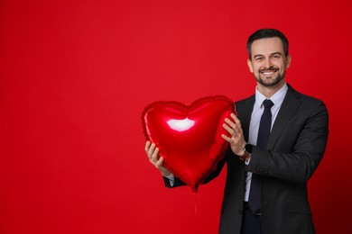 Photo of Happy Valentine's Day. Handsome man with heart shaped balloon on red background. Space for text