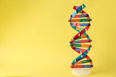 Photo of DNA structure model on yellow background, space for text