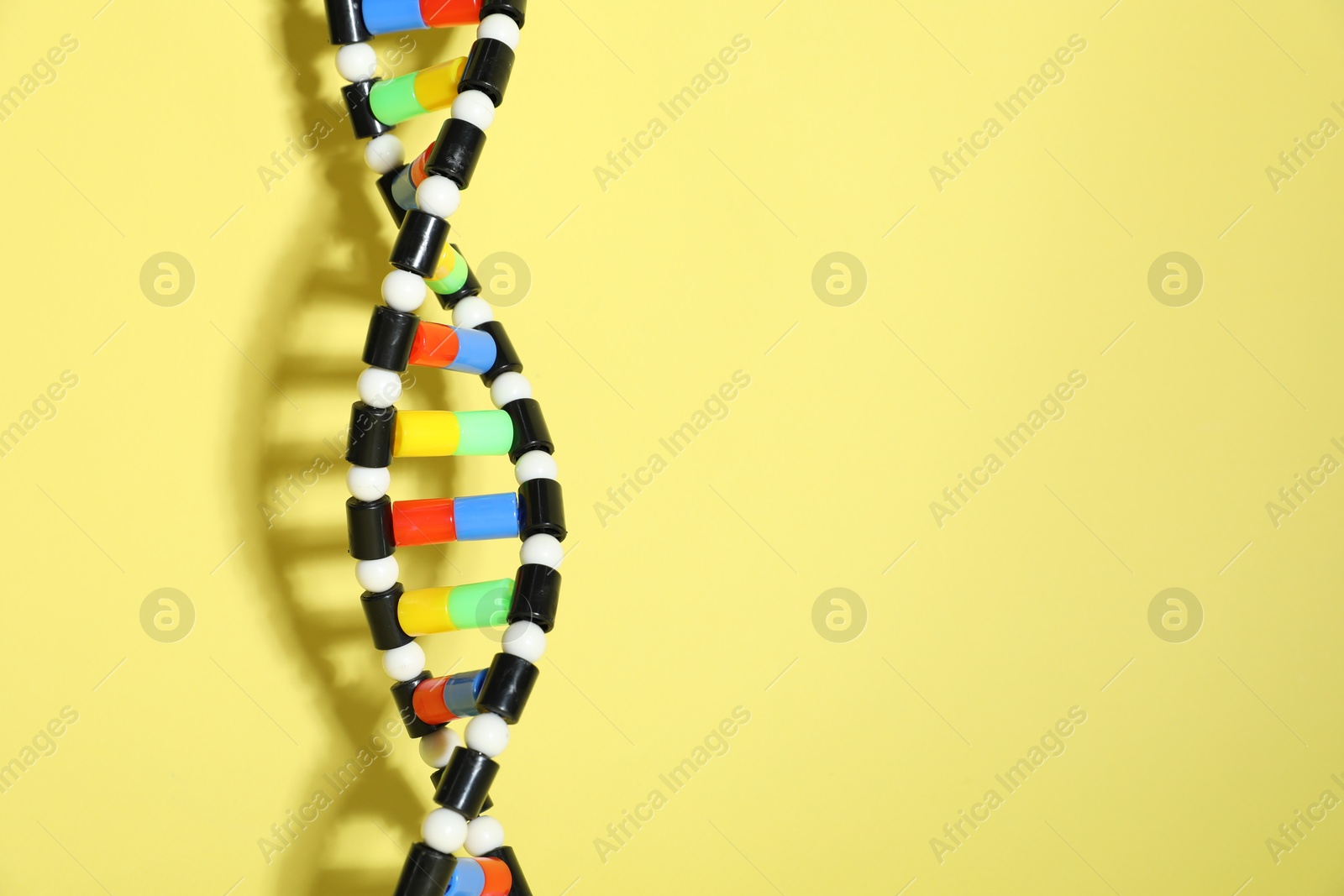 Photo of DNA structure model on yellow background, space for text