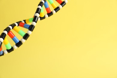 Photo of DNA structure model on yellow background, closeup. Space for text