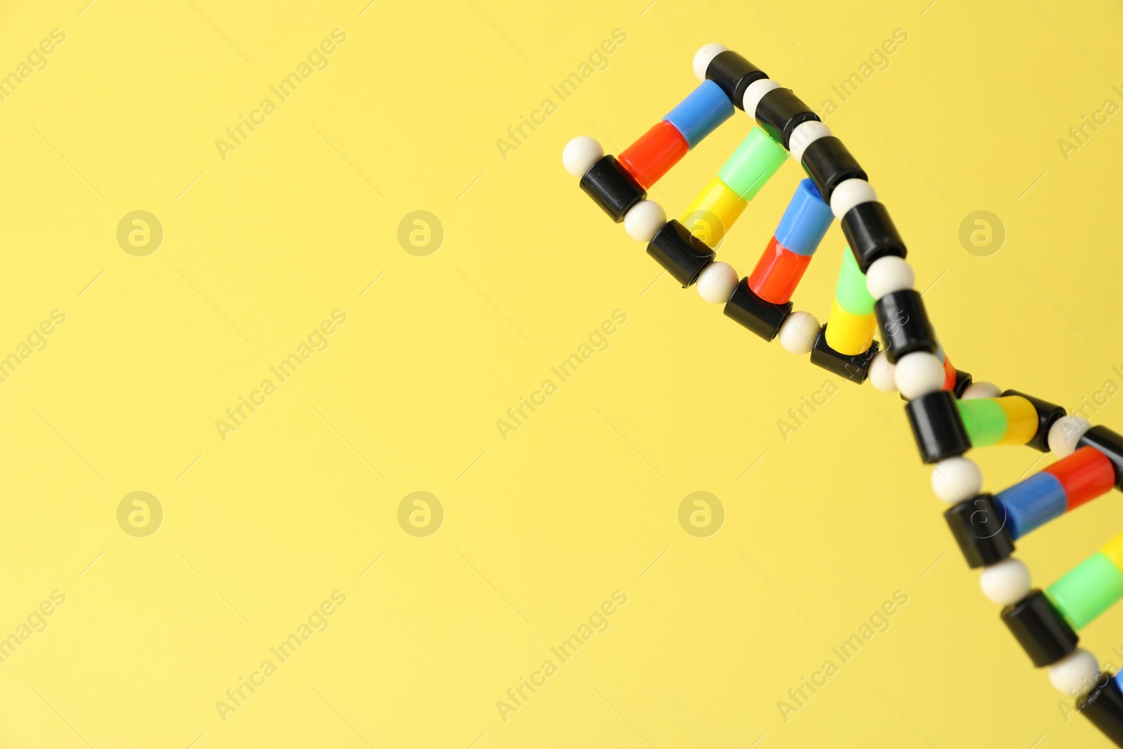 Photo of DNA structure model on yellow background, closeup. Space for text