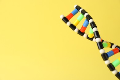 Photo of DNA structure model on yellow background, closeup. Space for text