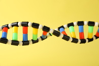 Photo of DNA structure model on yellow background, closeup