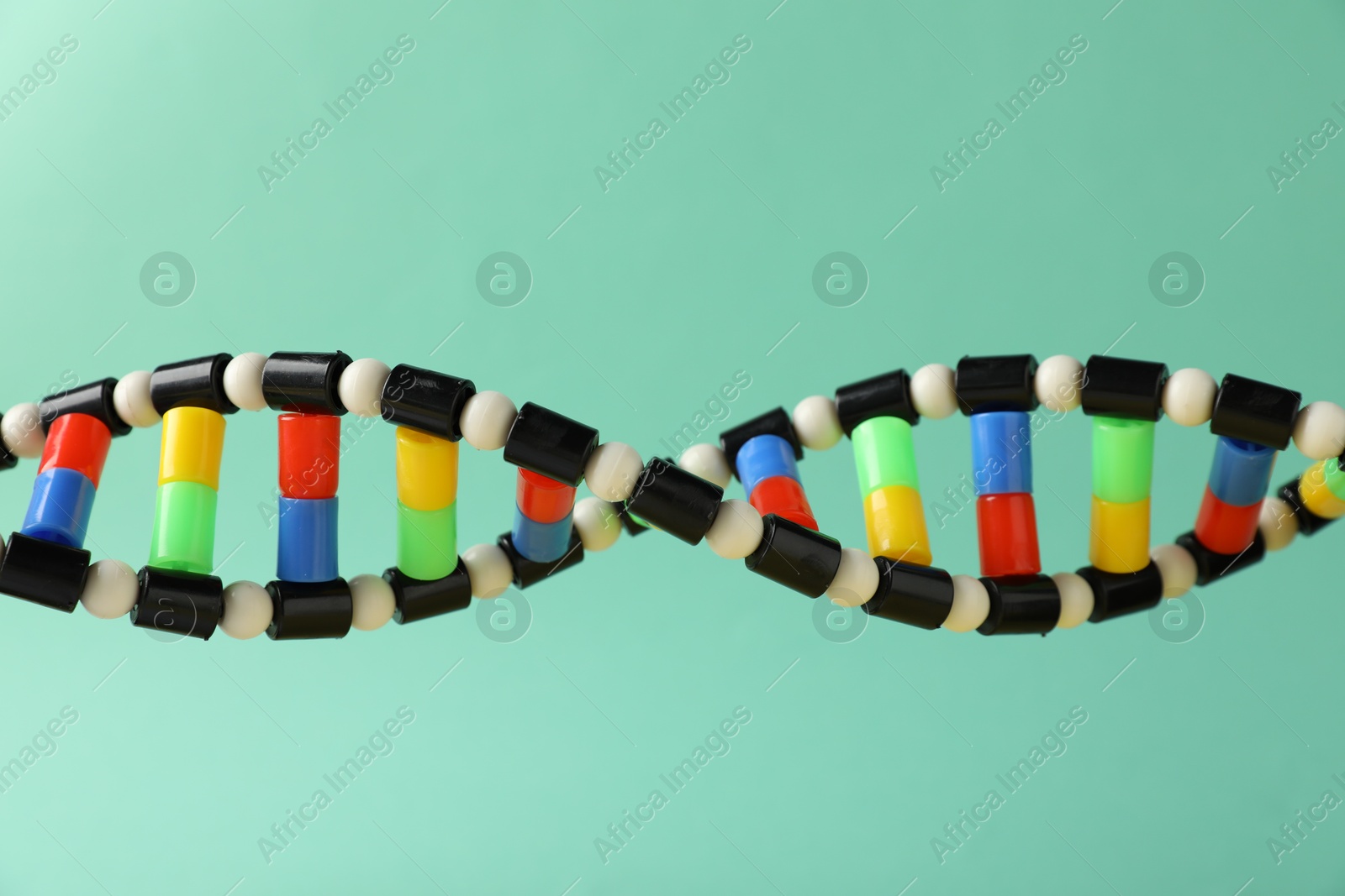 Photo of DNA structure model on turquoise background, closeup