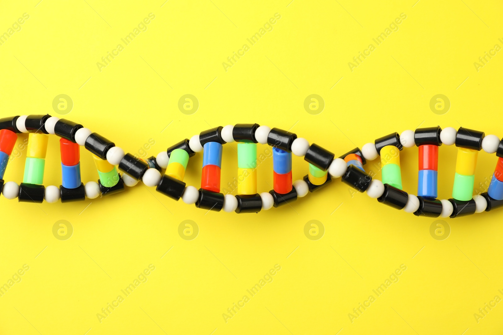 Photo of DNA structure model on yellow background, top view