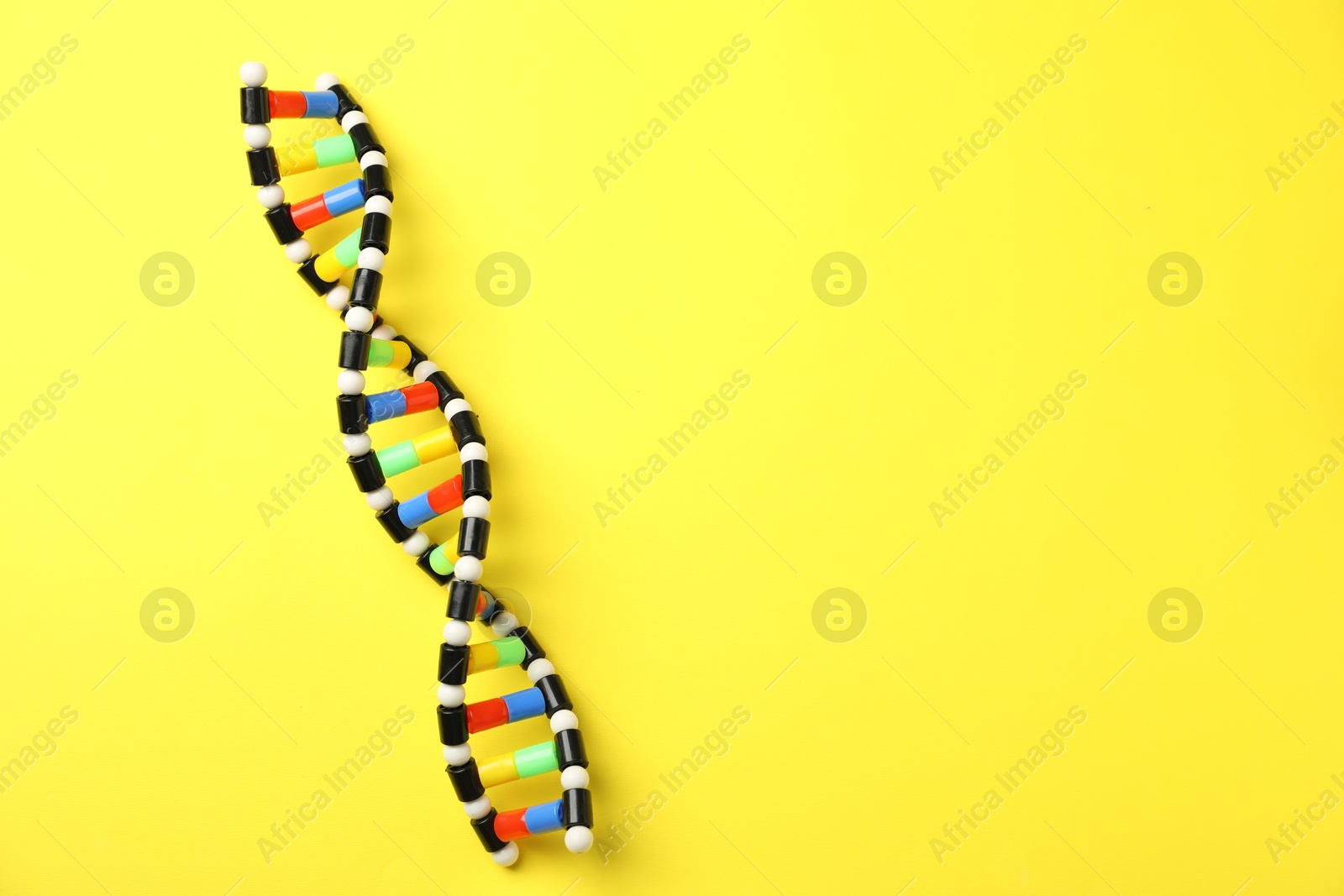 Photo of DNA structure model on yellow background, top view. Space for text