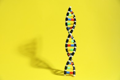 Photo of Colorful DNA structure model on yellow background. Space for text