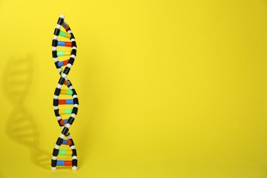 Photo of Colorful DNA structure model on yellow background. Space for text