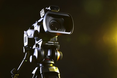 Modern video camera with tripod on black background, closeup. Space for text