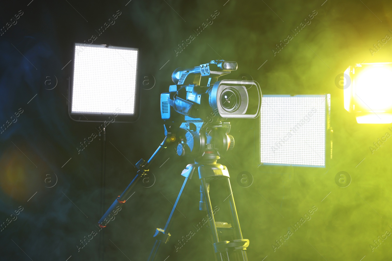 Photo of Modern video camera with tripod and lighting equipment in smoke on black background