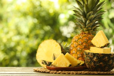 Photo of Fresh ripe pineapples on wooden table against blurred background, space for text