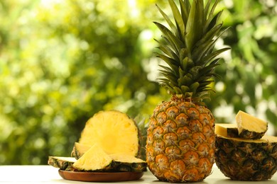 Photo of Fresh ripe pineapples on white wooden table against blurred background