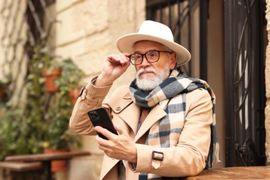 Photo of Stylish senior man with smartphone in outdoor bar