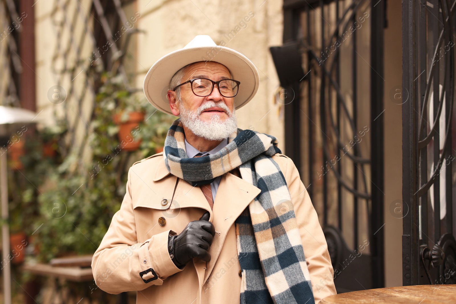 Photo of Stylish senior man with hat and scarf in outdoor bar