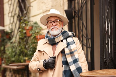 Stylish senior man with hat and scarf in outdoor bar